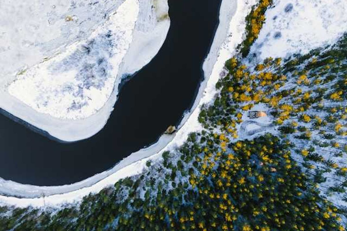 A aerial view of water, snow, and forested land