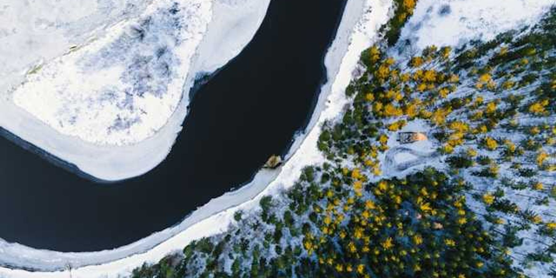 A aerial view of water, snow, and forested land