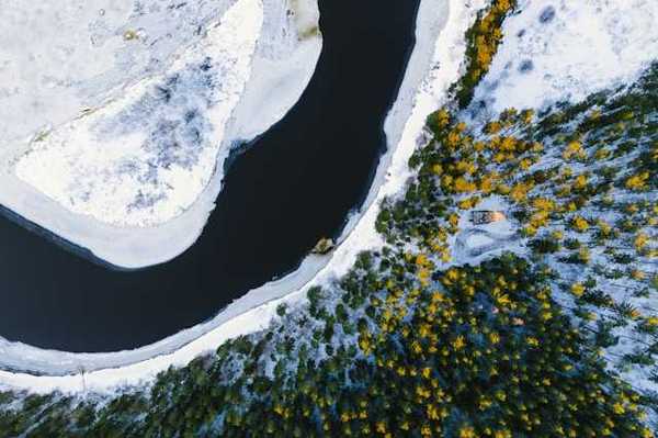 A aerial view of water, snow, and forested land