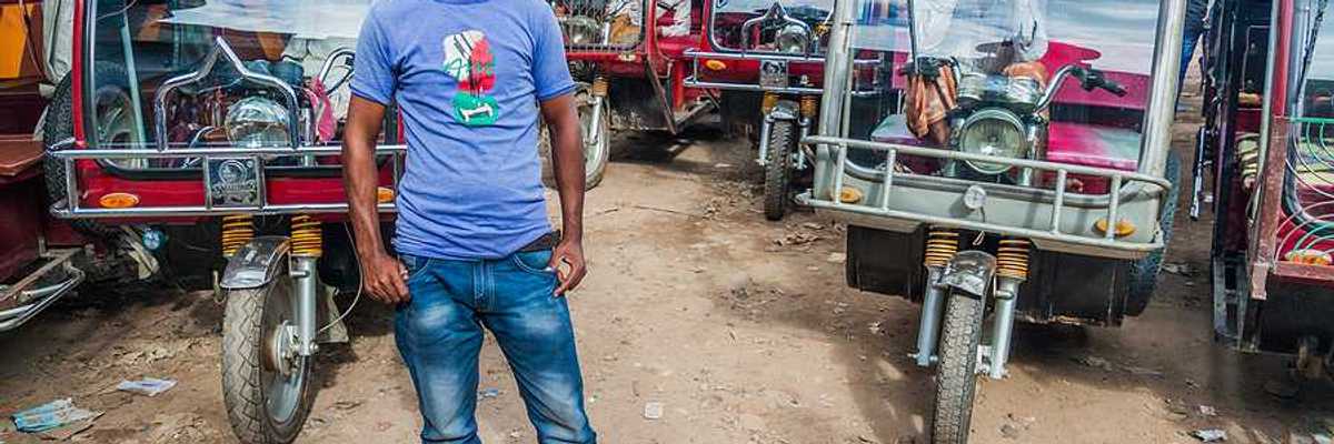 A Bangladeshi man standing in front of a group of motorcycle-powered rickshaws