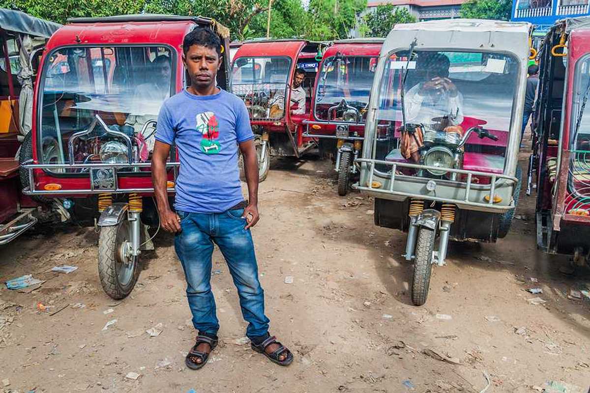 A Bangladeshi man standing in front of a group of motorcycle-powered rickshaws