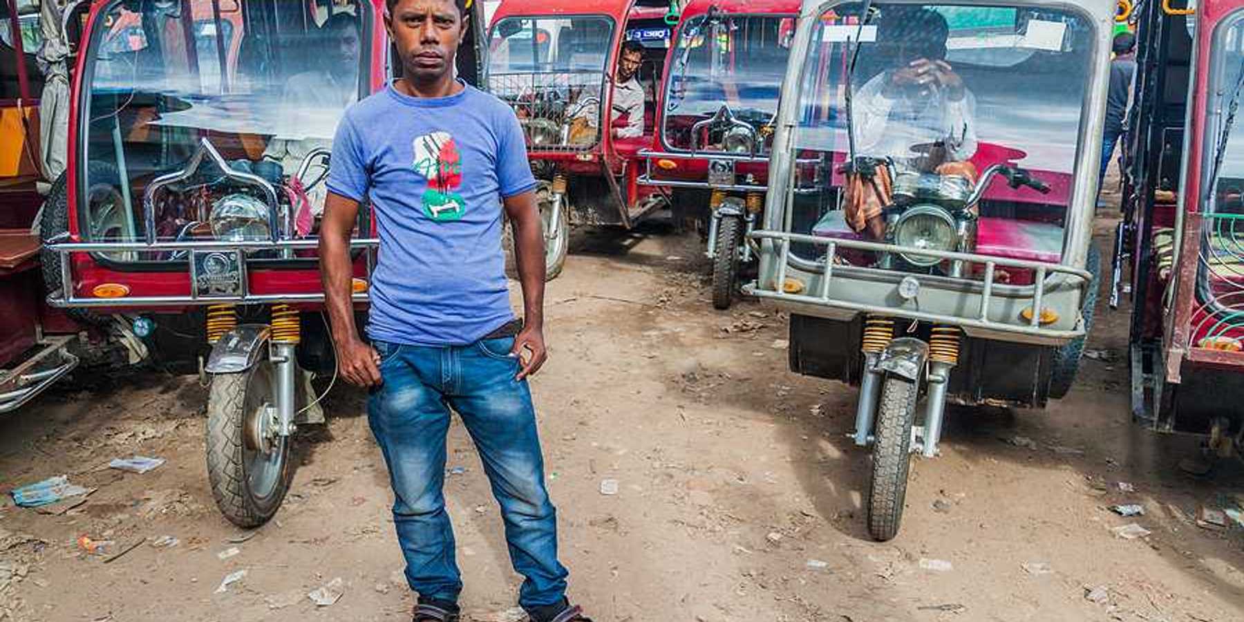A Bangladeshi man standing in front of a group of motorcycle-powered rickshaws