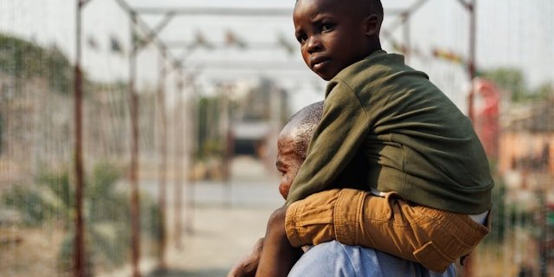 A black child looking at the camera being carried on a man's shoulders.
