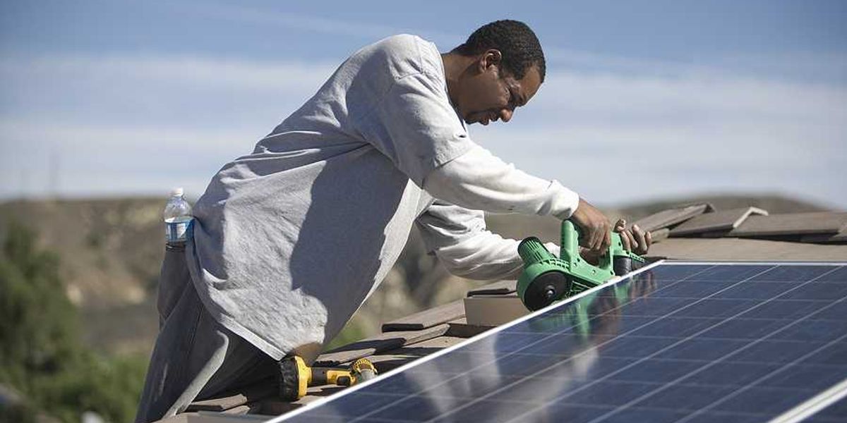 A black man installing solar panels on a roof on a sunny day