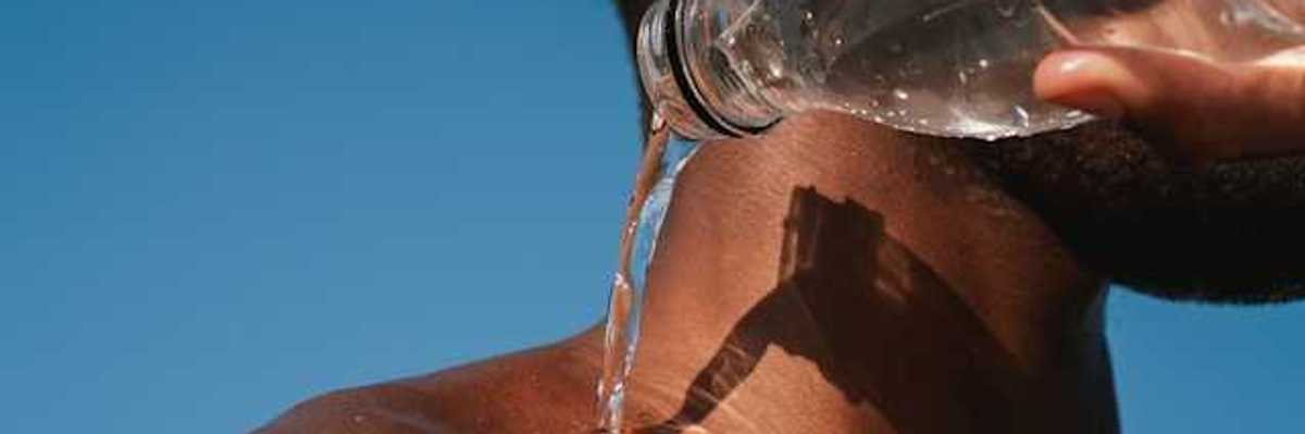 A Black man pouring a bottle of water on his shoulder on a hot day