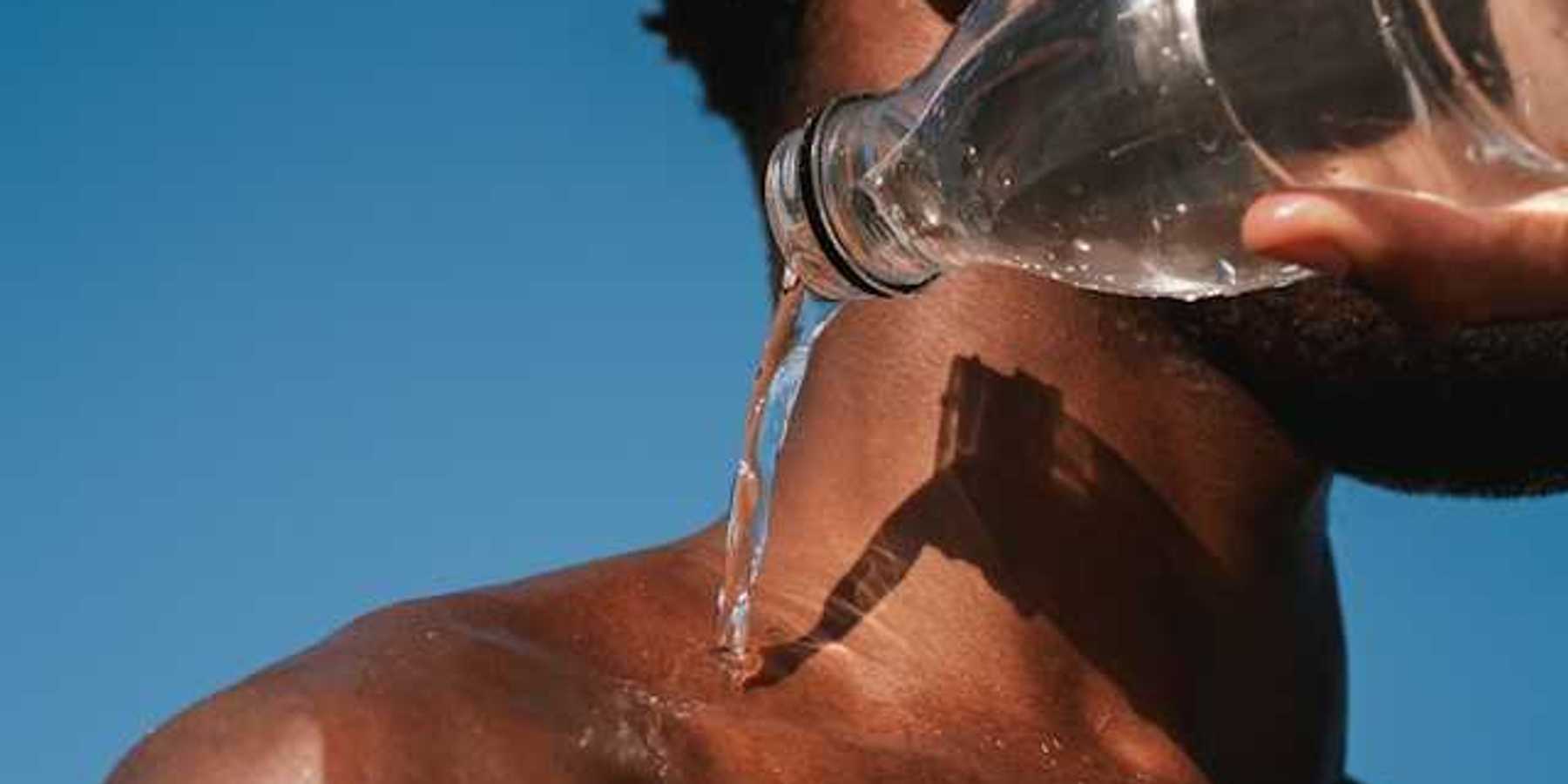 A Black man pouring a bottle of water on his shoulder on a hot day