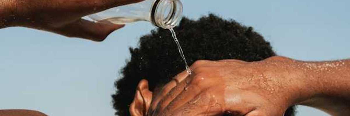 A Black man pouring water on his neck on a hot day