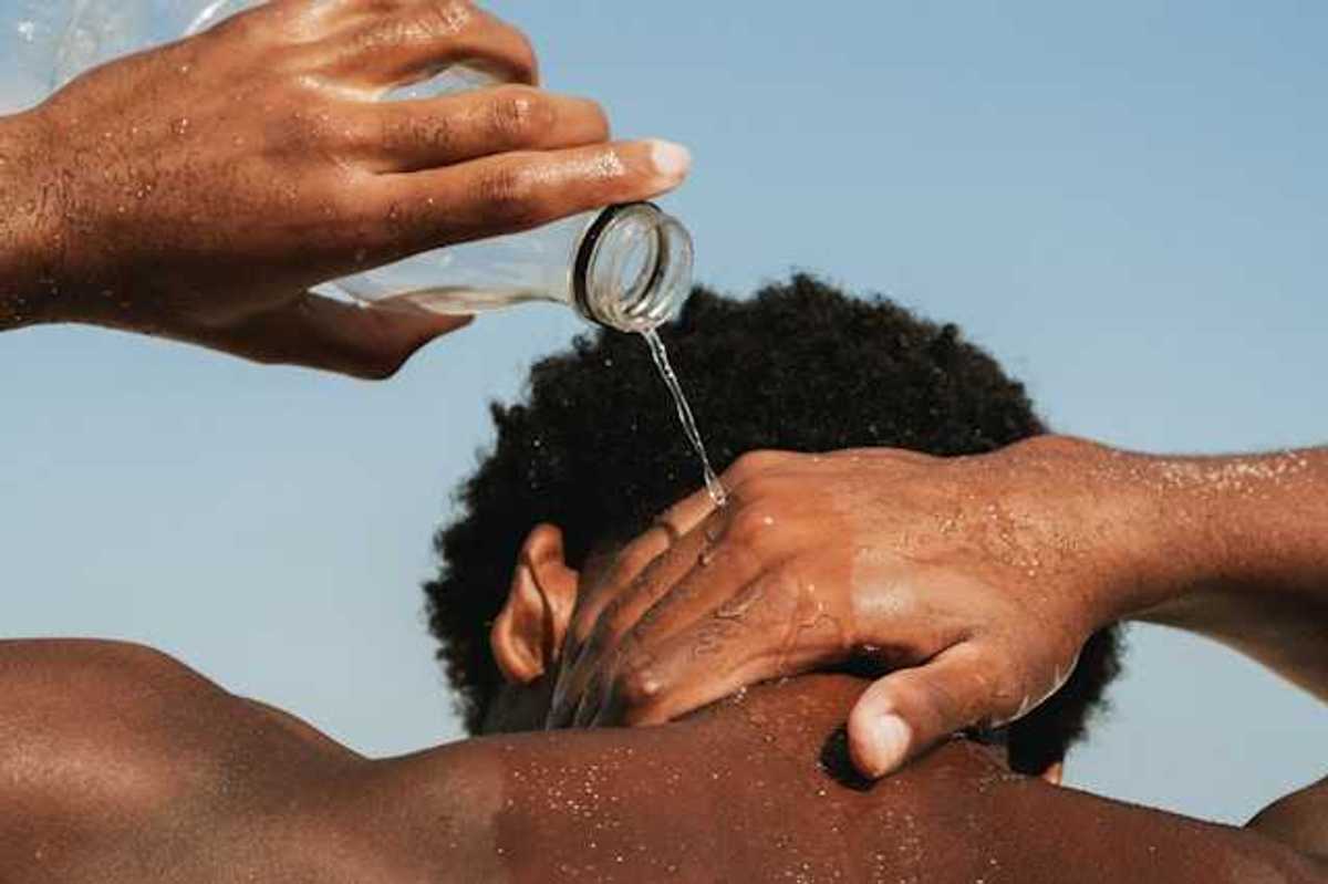 A Black man pouring water on his neck on a hot day
