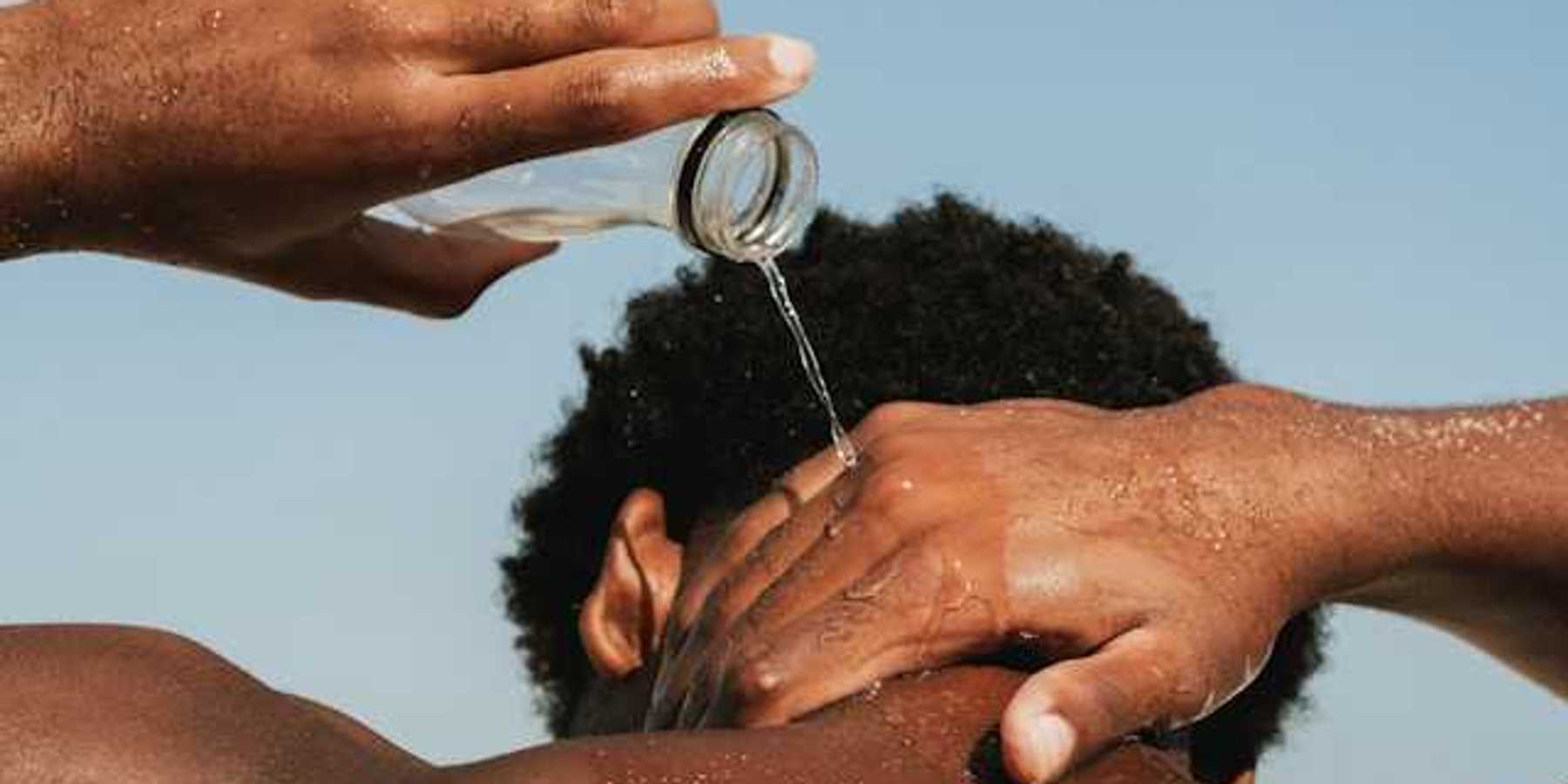 A Black man pouring water on his neck on a hot day