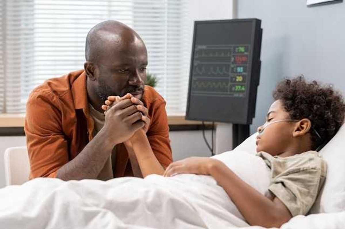 A Black man sitting at the hospital bedside of his son