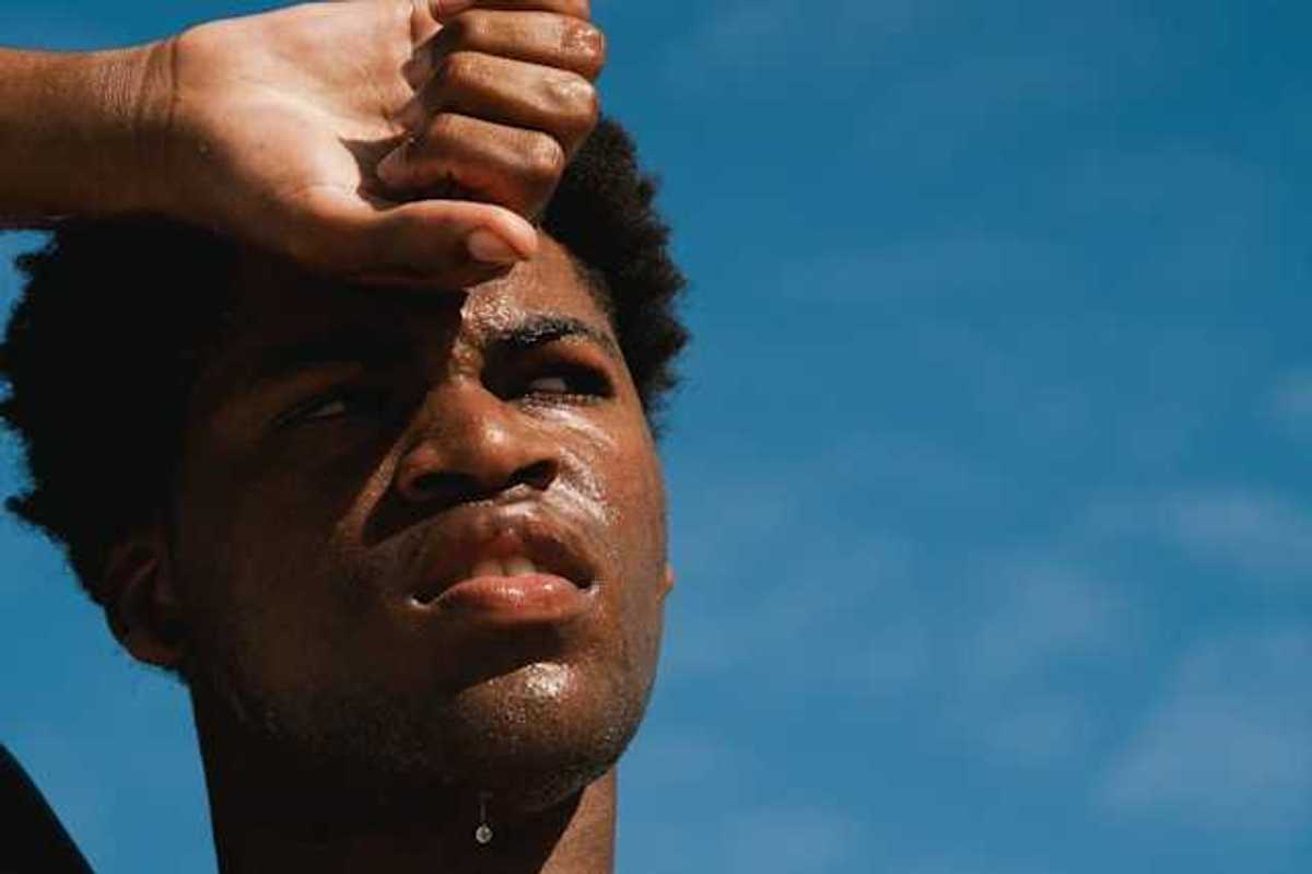A Black man with perspiration on his face on a sunny day