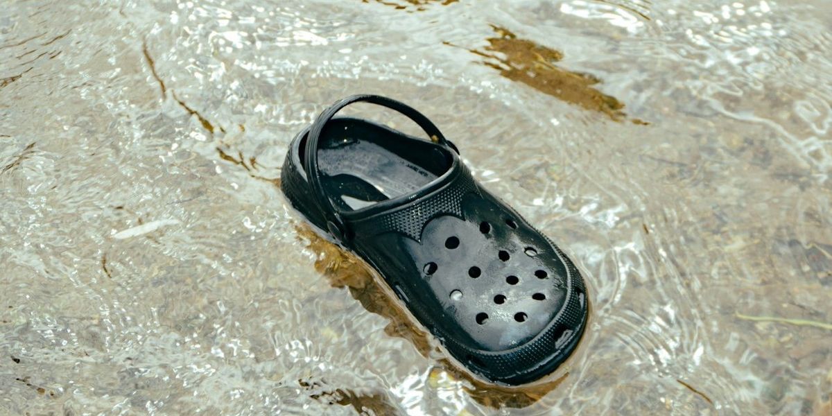 A black plastic Crocs shoe floats in floodwaters.