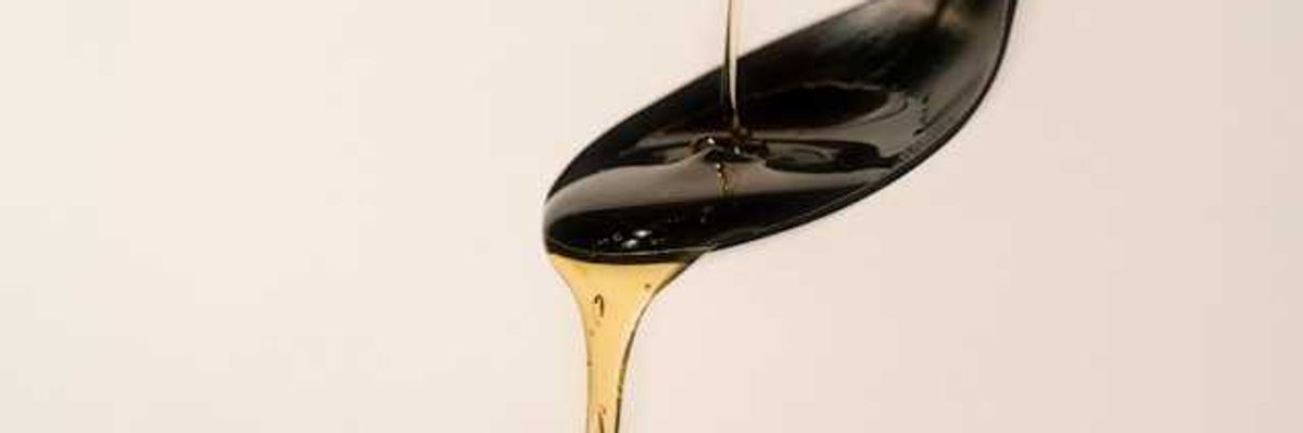 A black spoon with amber colored oil flowing over it
