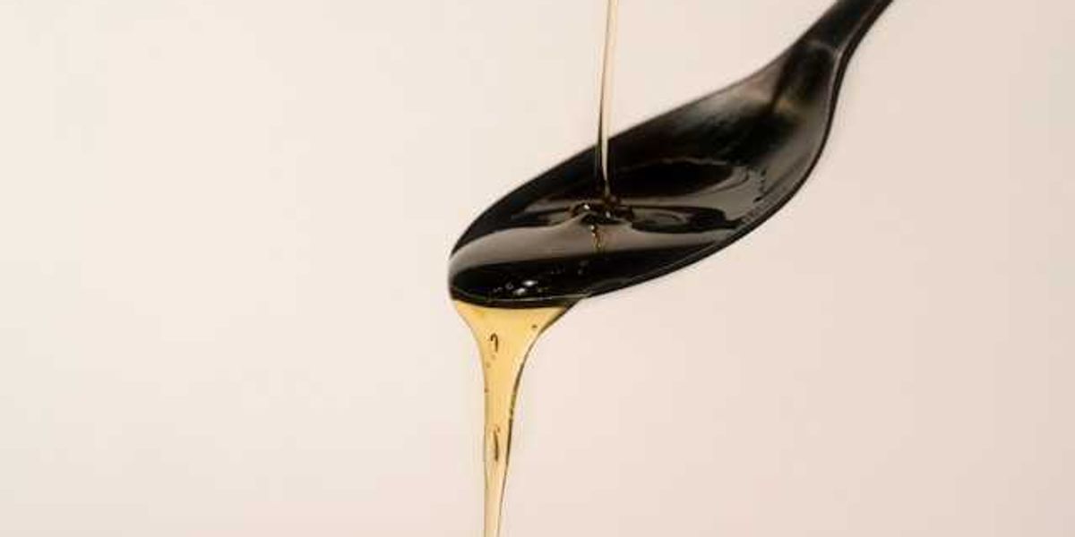 A black spoon with amber colored oil flowing over it