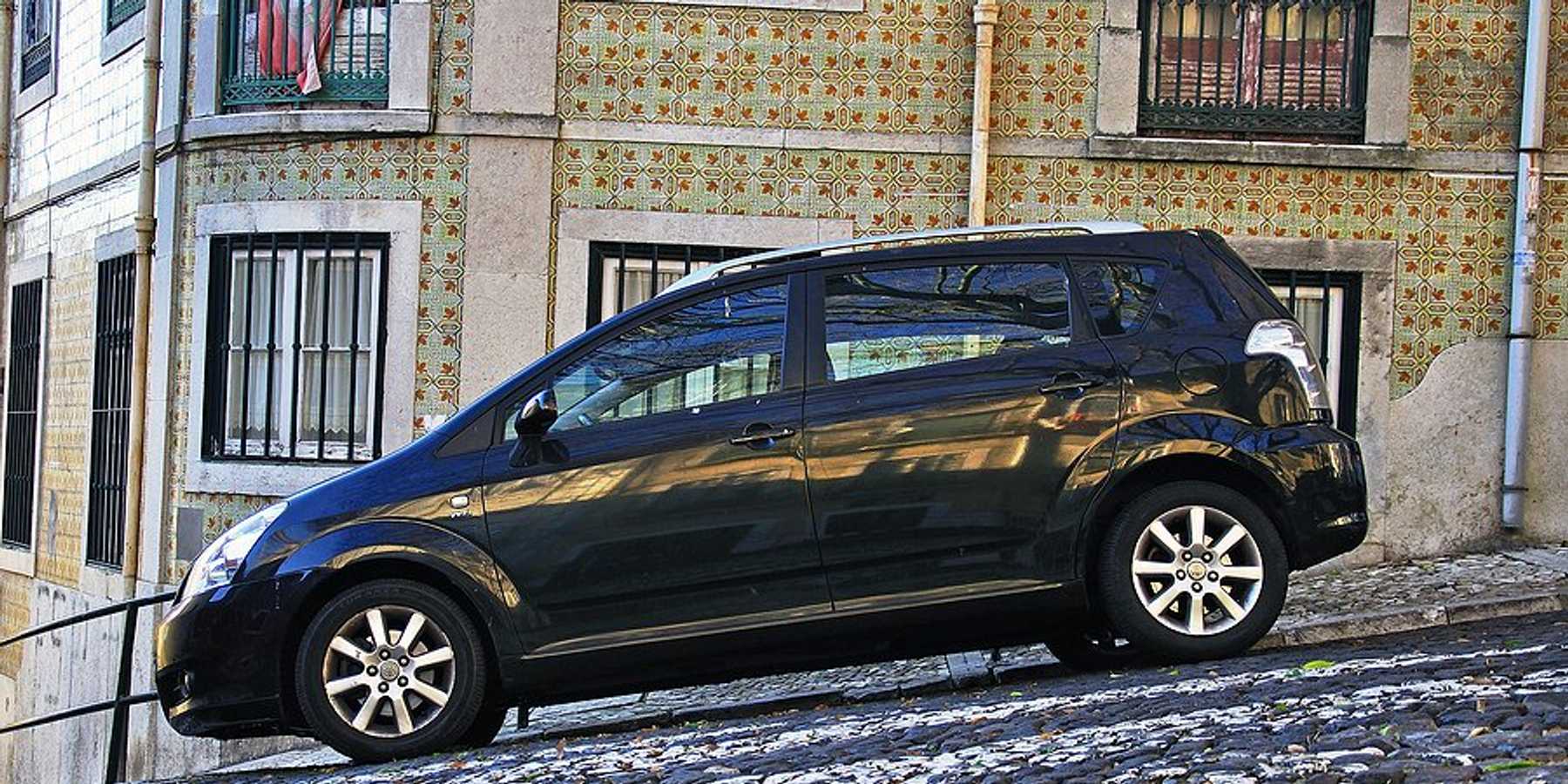 A black station wagon parked on a Lisbon street with a colorfully tiled house in the background.