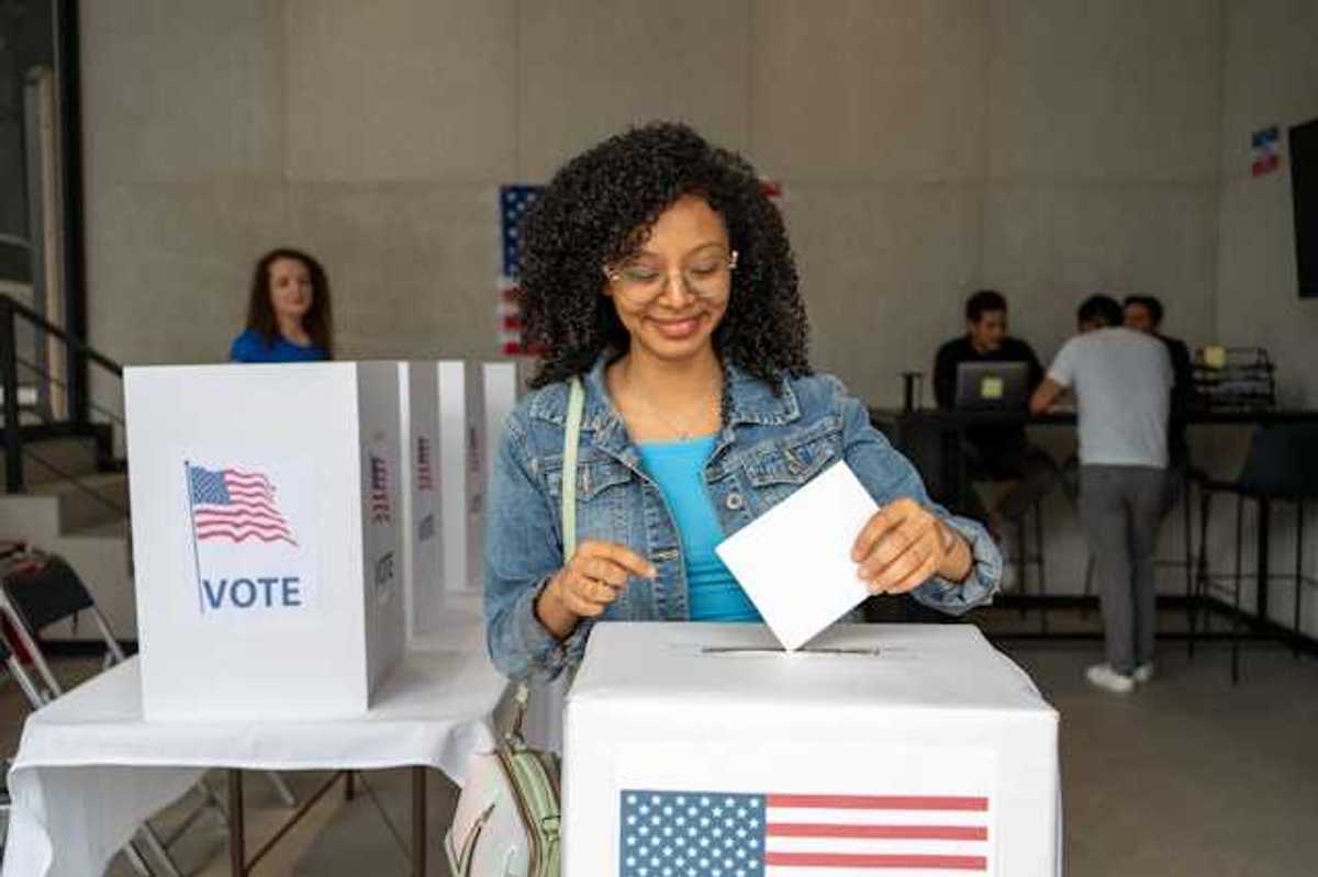 A Black woman putting her voting record into a box at a polling station