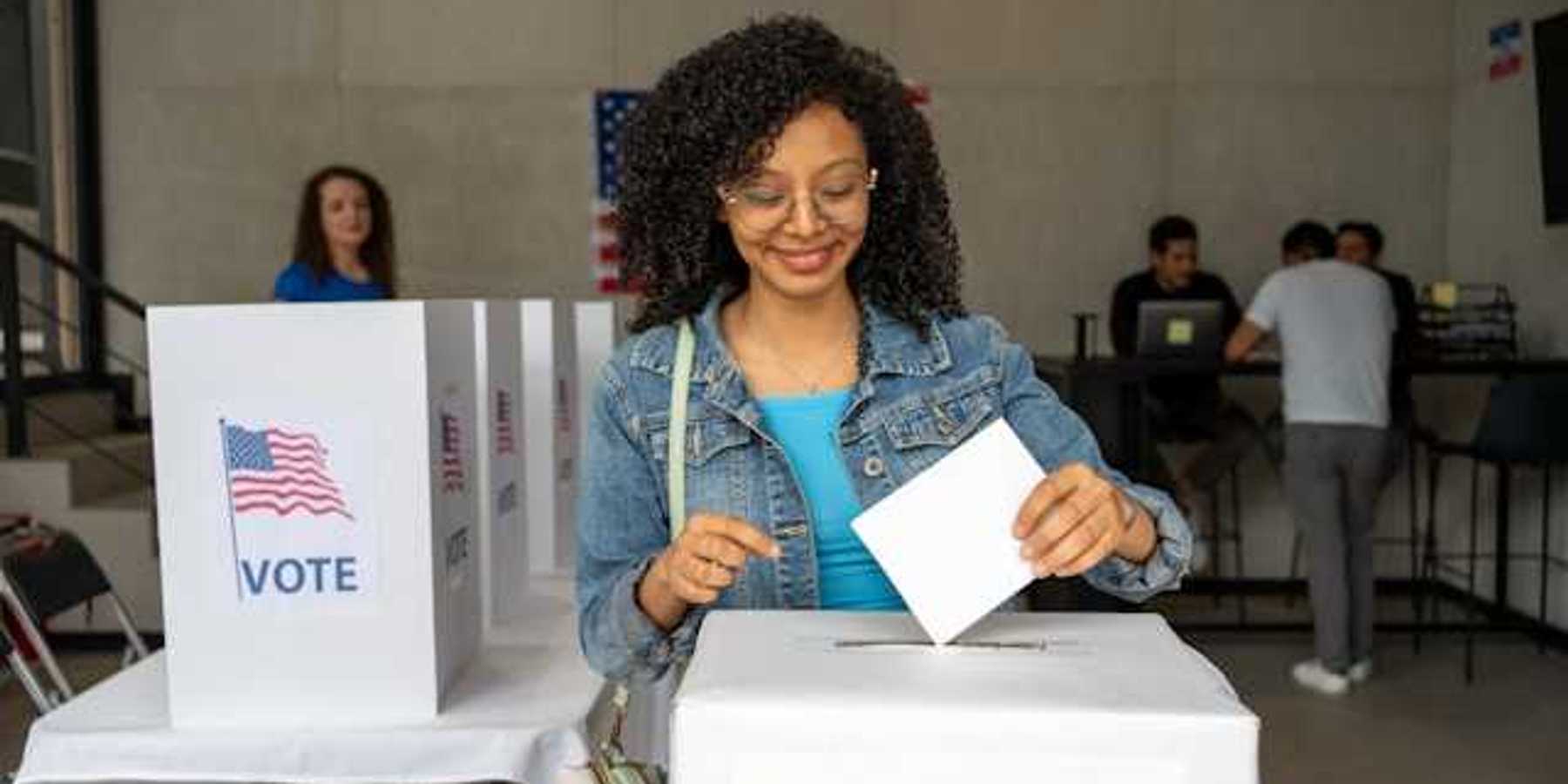 A Black woman putting her voting record into a box at a polling station