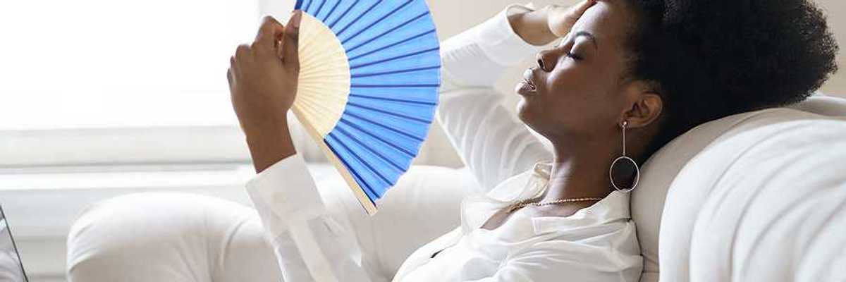 A Black woman sitting on a sofa with a blue hand fan