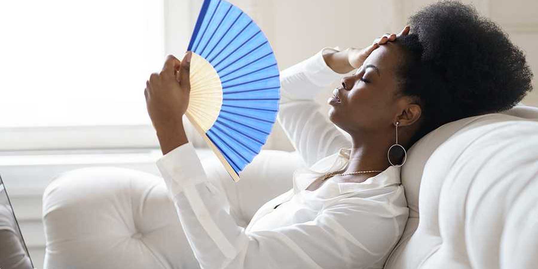 A Black woman sitting on a sofa with a blue hand fan