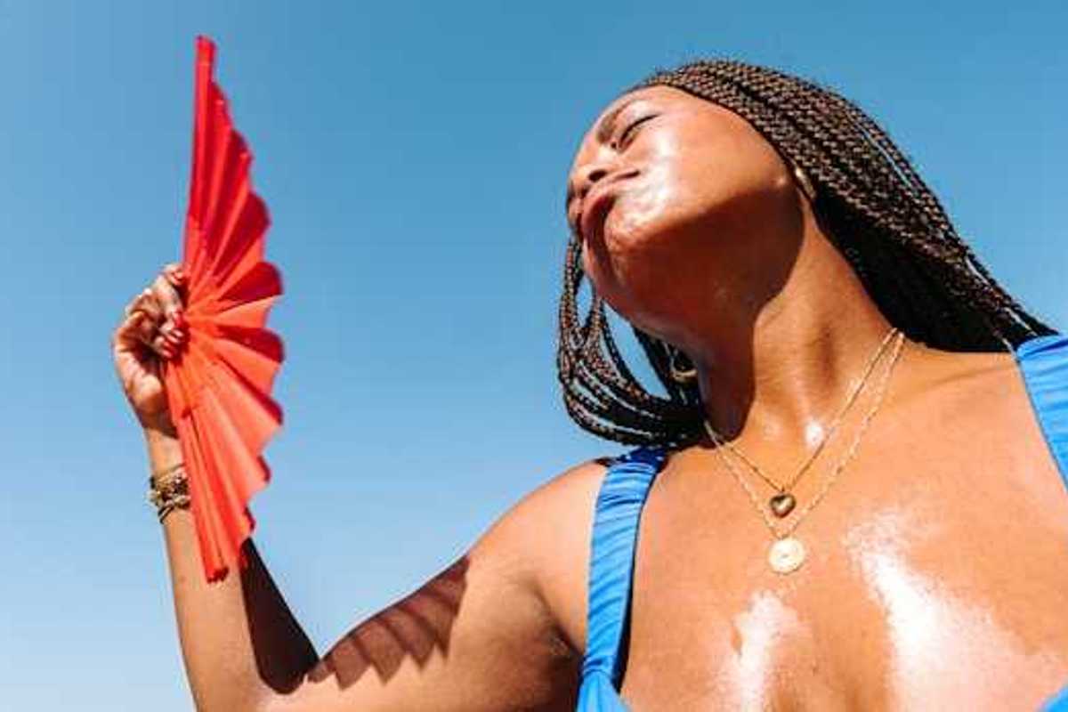 A Black woman using a red fan to cool her face on a hot day