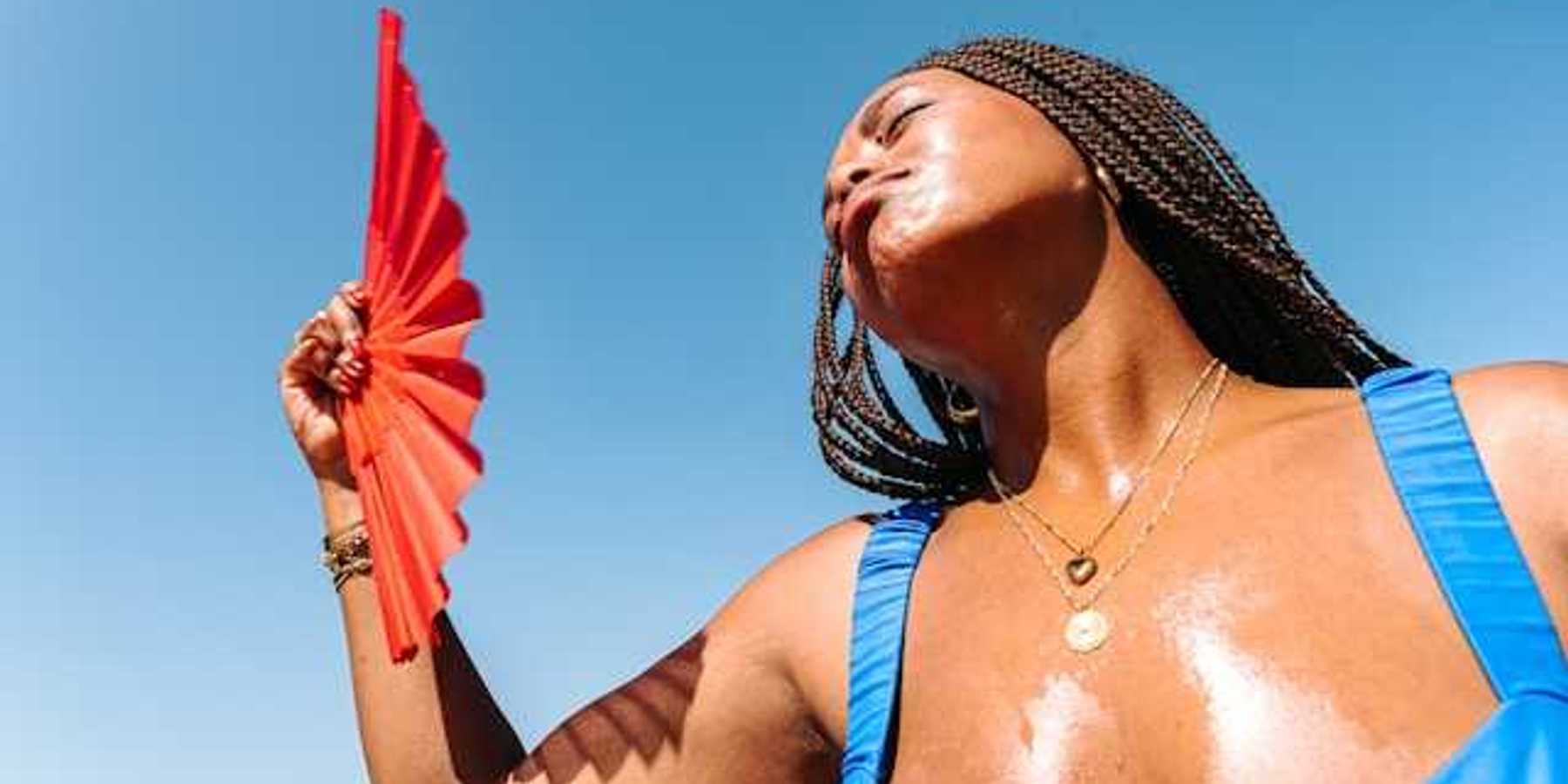 A Black woman using a red fan to cool her face on a hot day