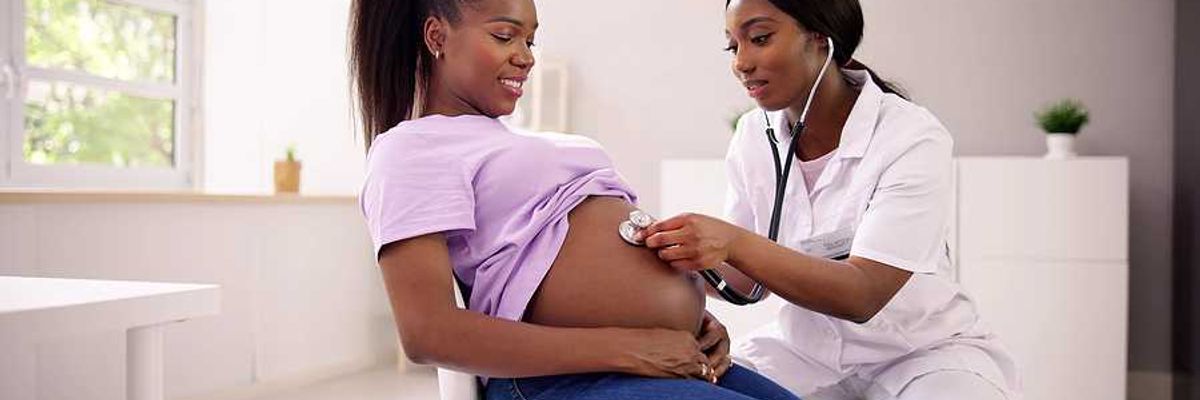 A Black woman with a stethoscope listening to the pregnant belly of another Black woman