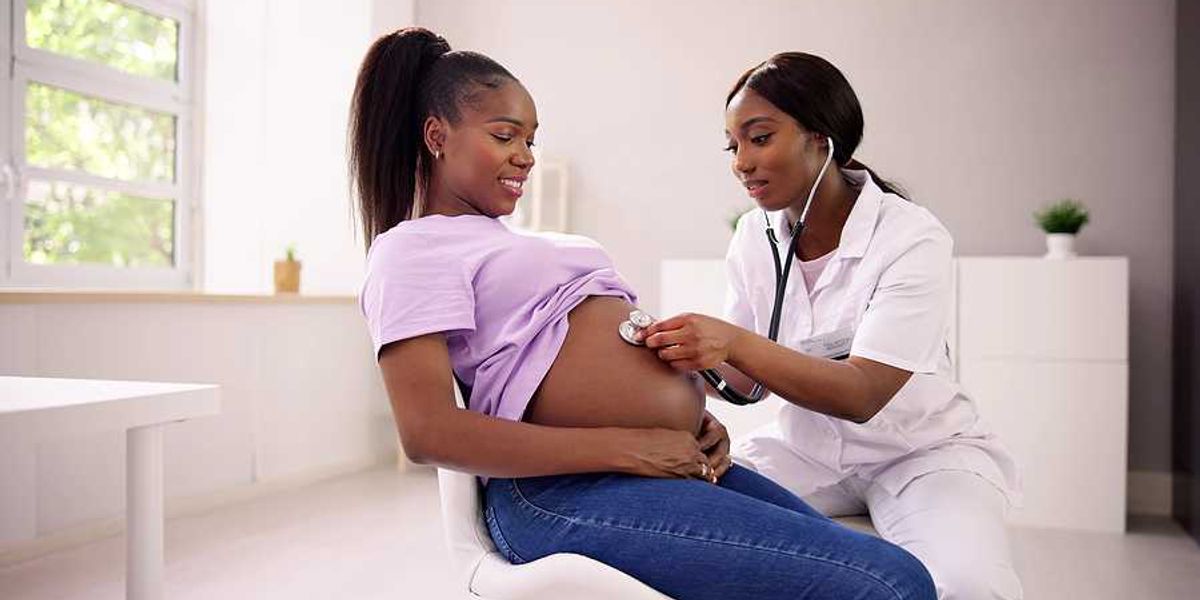 A Black woman with a stethoscope listening to the pregnant belly of another Black woman