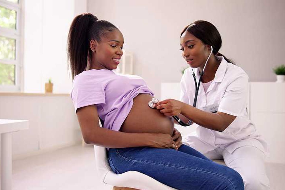 A Black woman with a stethoscope listening to the pregnant belly of another Black woman
