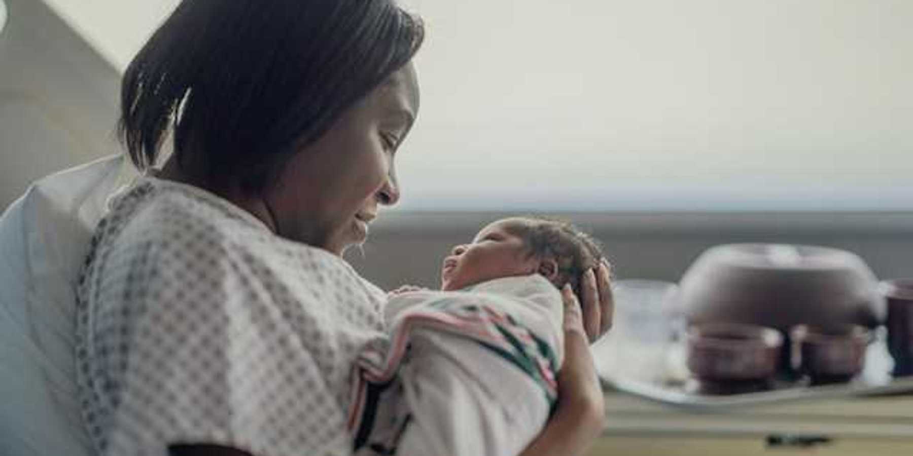 A Black women holding her newborn infant in a hospital room