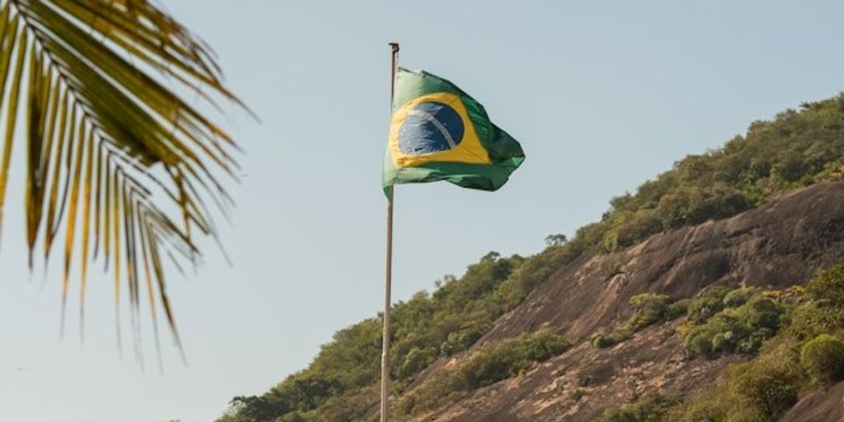 A Brazilian flag flying over a green hill.