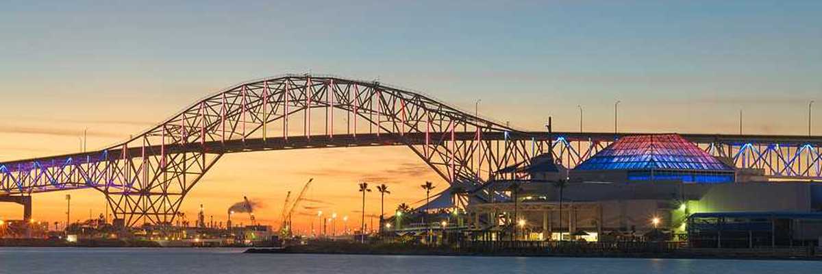 A bridge extending over a body of water with buildings and docks in the background at sunset