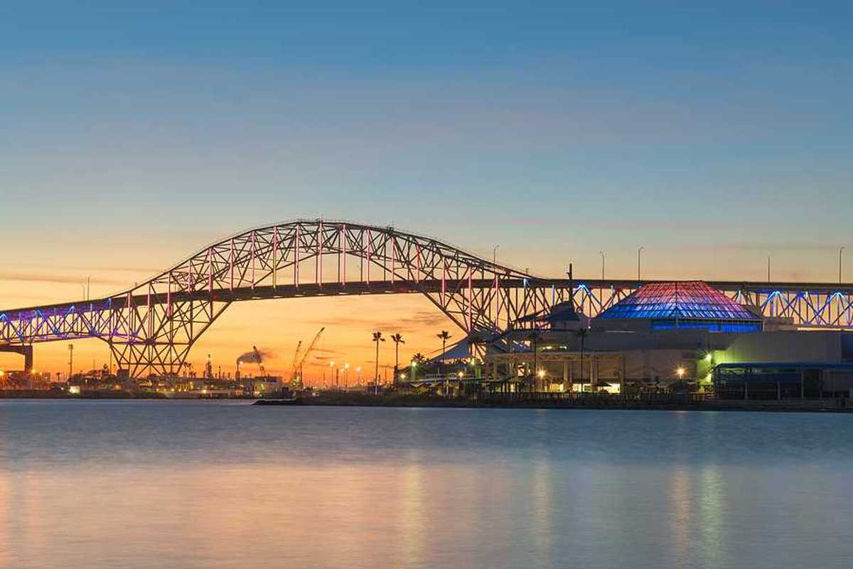 A bridge extending over a body of water with buildings and docks in the background at sunset