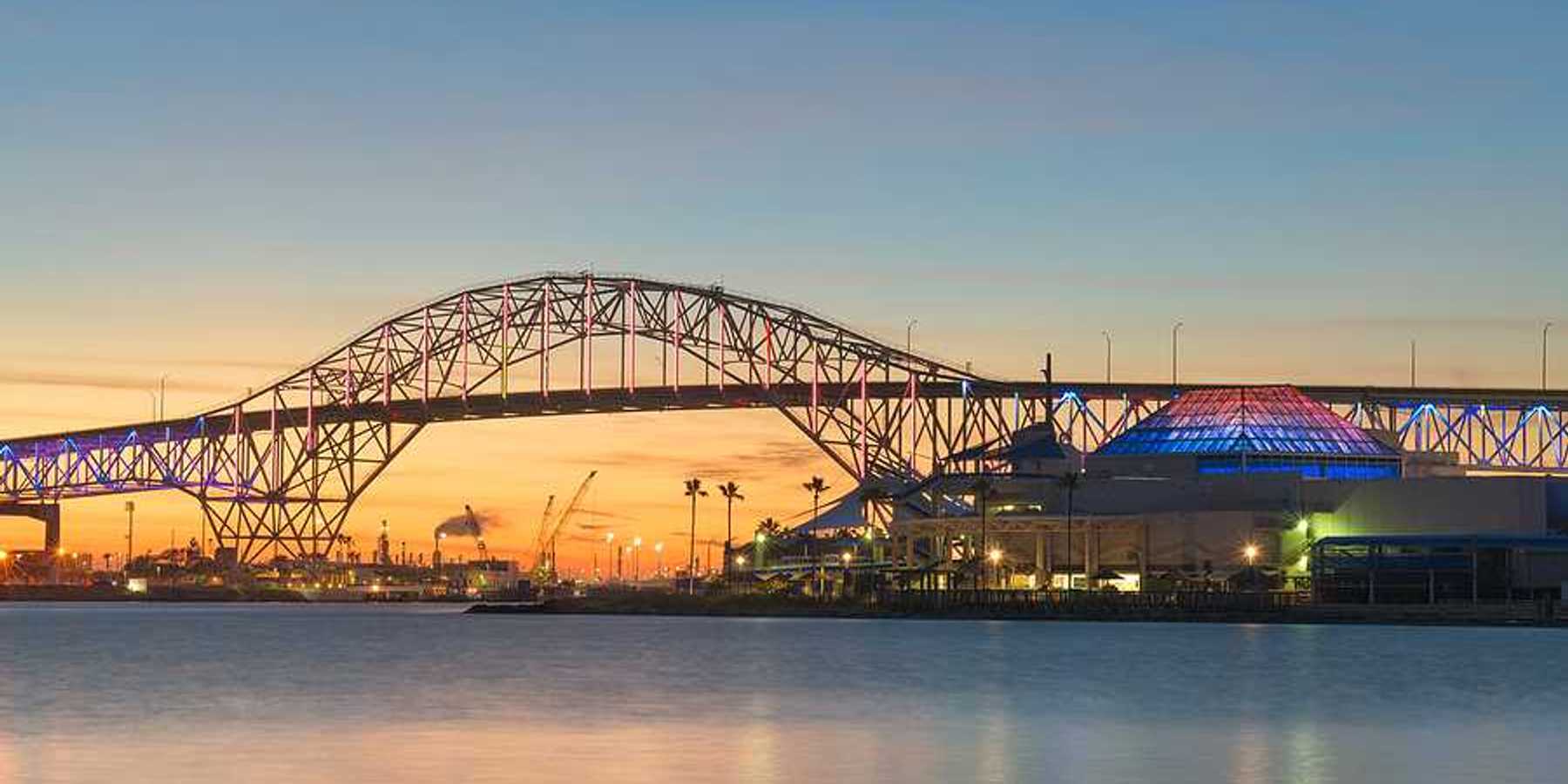 A bridge extending over a body of water with buildings and docks in the background at sunset