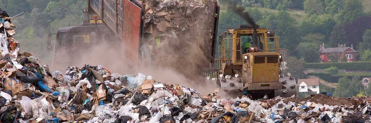 A bulldozer moving garbage on a landfill waste site as a garbage truck offloads more