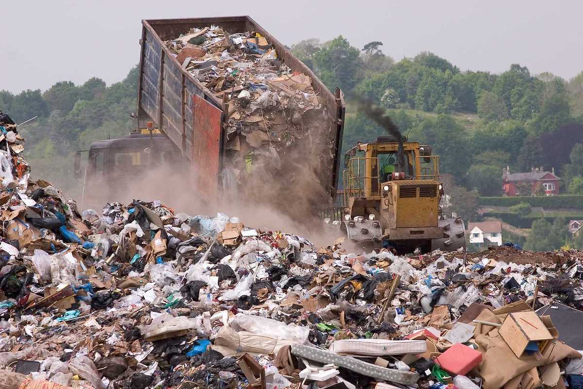A bulldozer moving garbage on a landfill waste site as a garbage truck offloads more