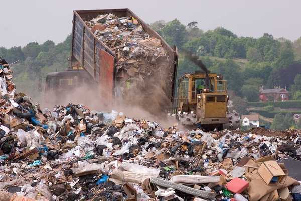 A bulldozer moving garbage on a landfill waste site as a garbage truck offloads more
