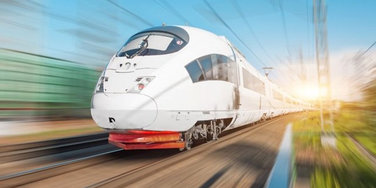 A bullet train speeding down the track with blurred landscape around it.