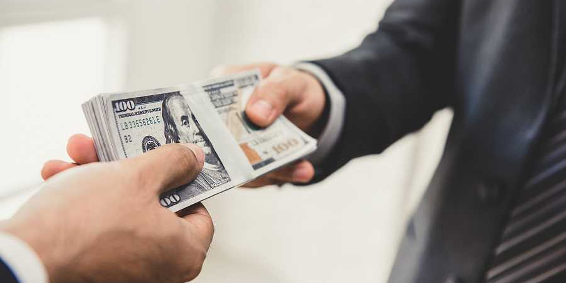 A businessman handing US hundred dollar bill over to another businessman
