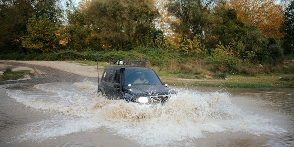 A car driving through a flooded street with trees in background.