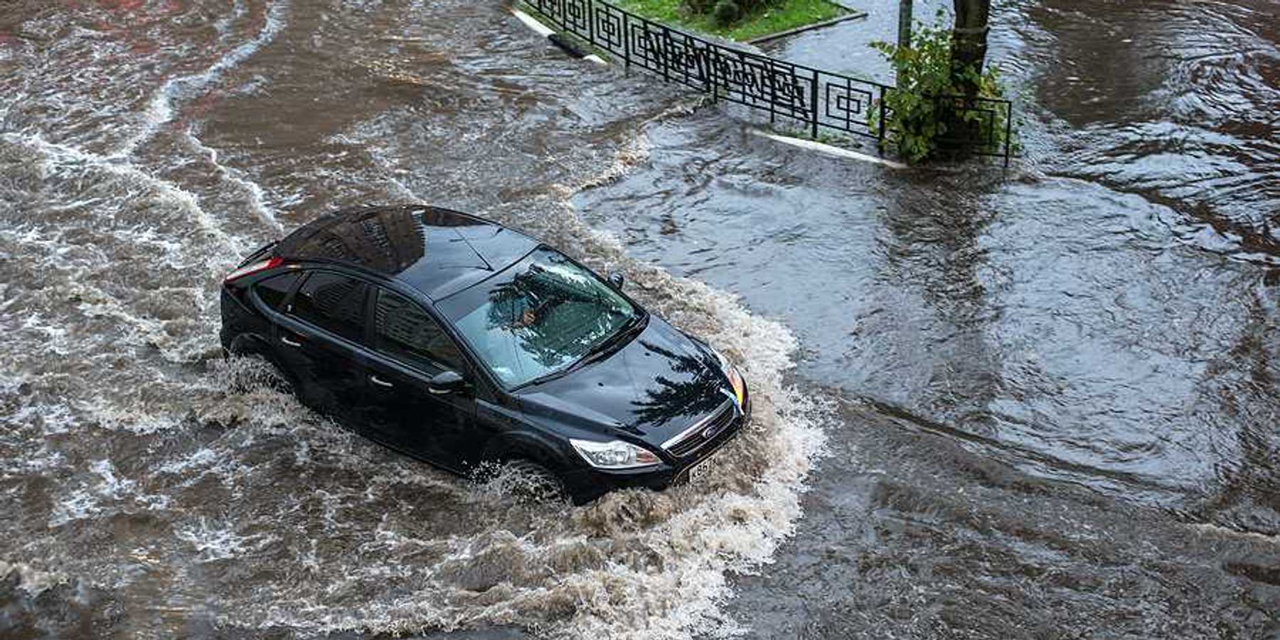A car driving through floodwaters in a city after a heavy rain