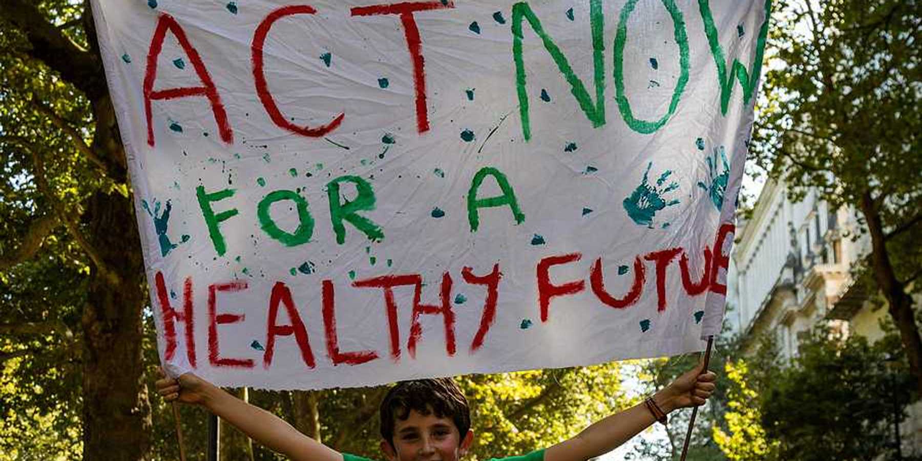 A child holding a protest sign that says Act Now for a Healthy Future