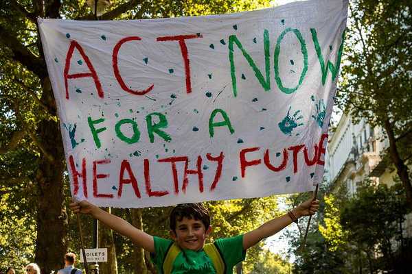 A child holding a protest sign that says Act Now for a Healthy Future