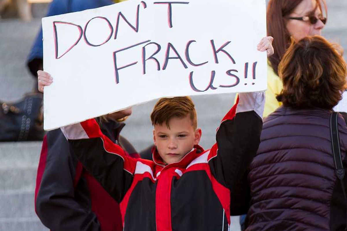 A child holding a protest sign that says Don't Frack Us!!