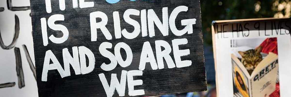 A child holding a protest sign that says 'the ocean is rising and so are we'
