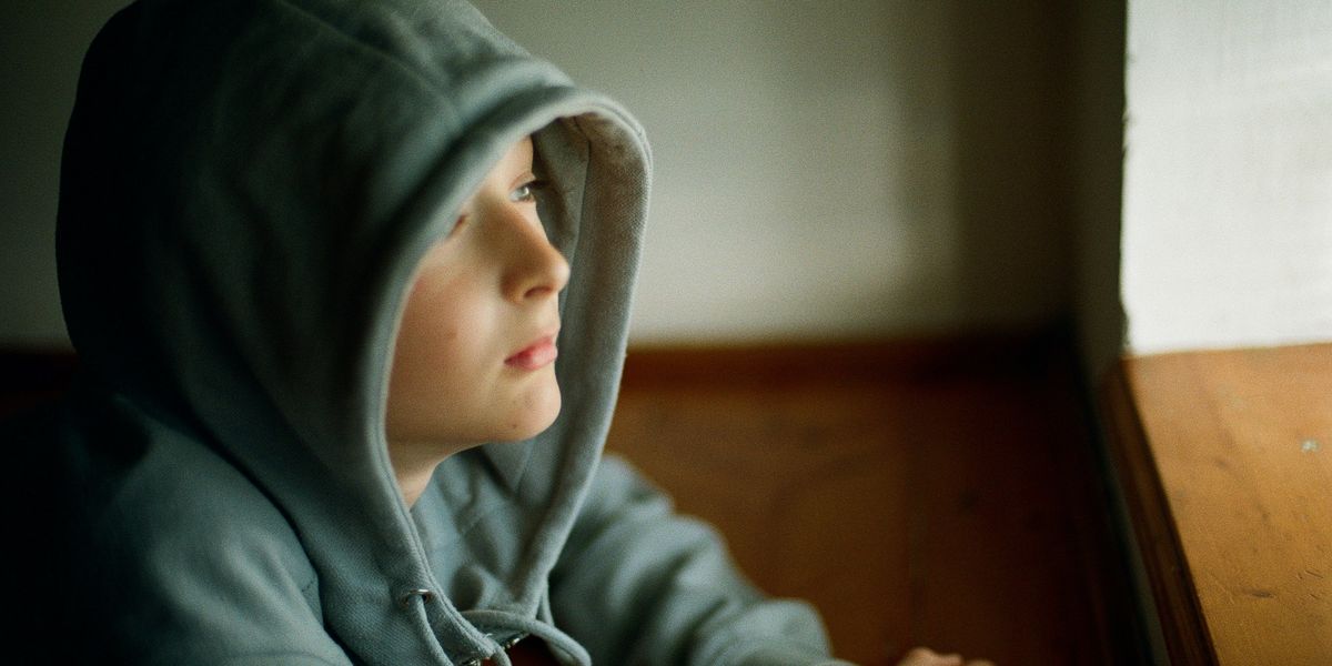 A child in a hooded sweatshirt looking out a window.