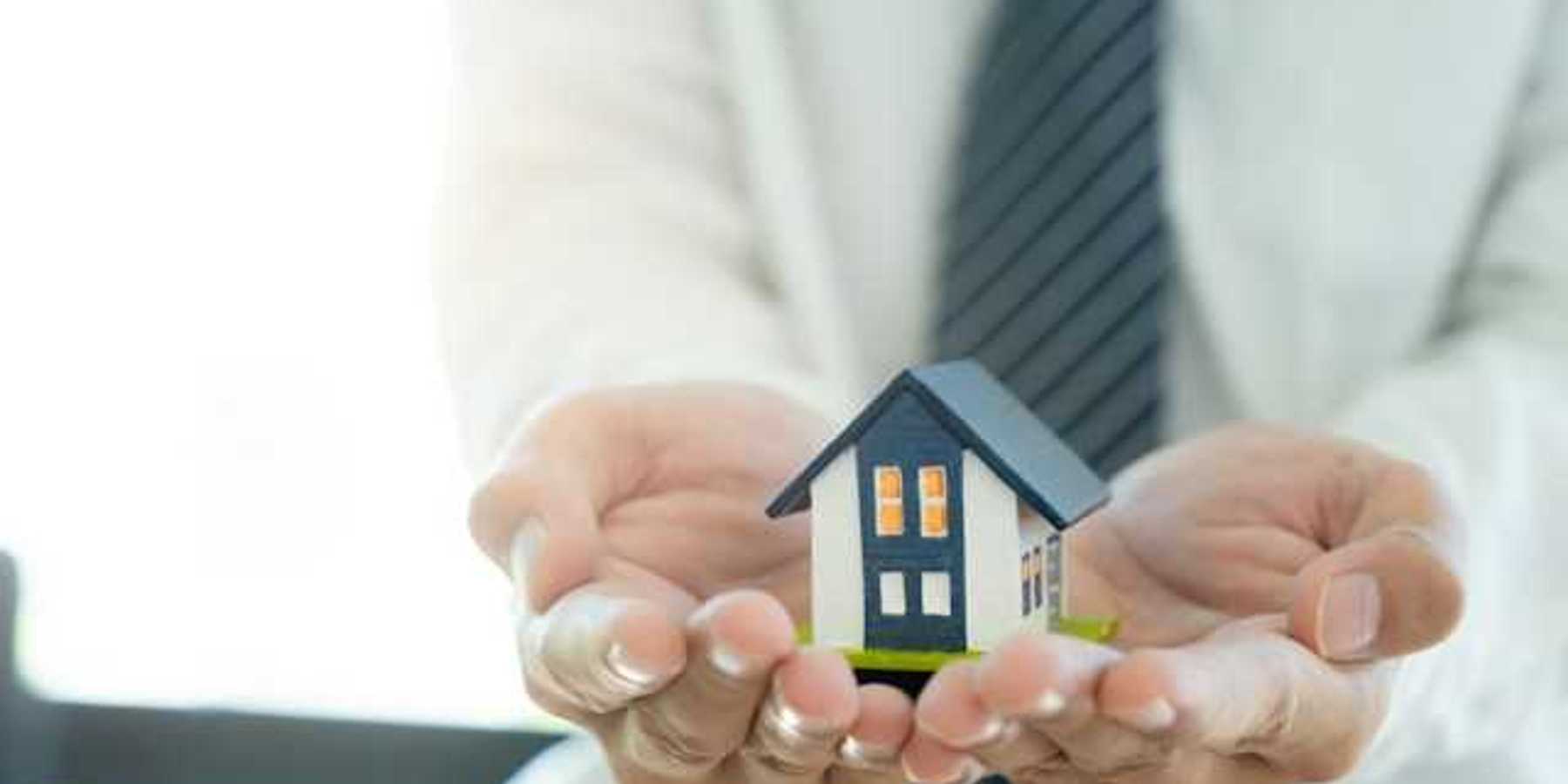 A closeup of a person's hands holding a miniature model of a house
