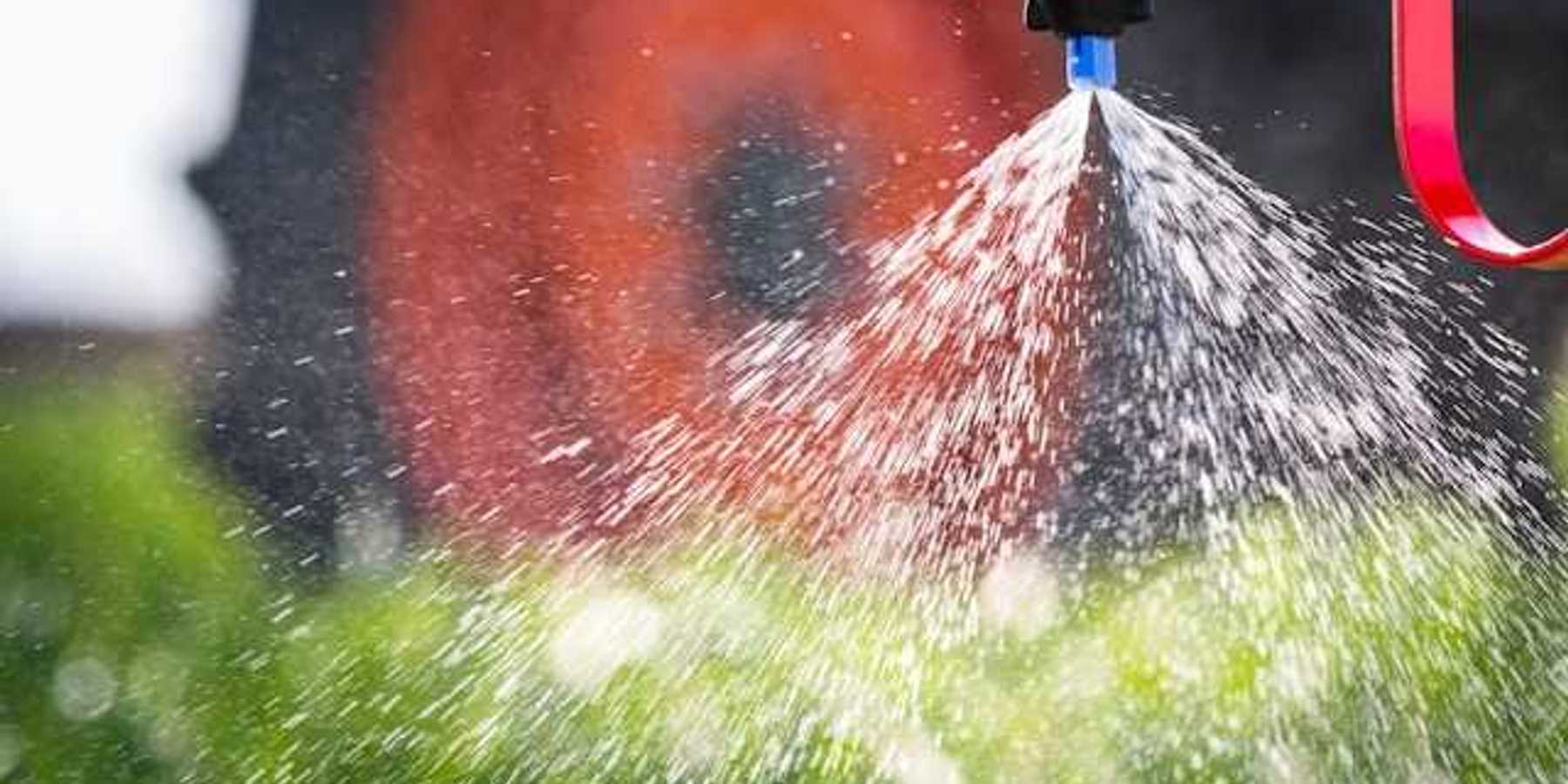 A closeup of a tractor implement spraying pesticides on a field