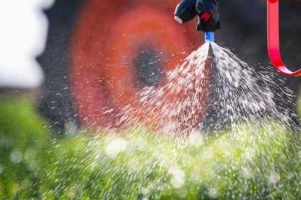 A closeup of a tractor implement spraying pesticides on a field