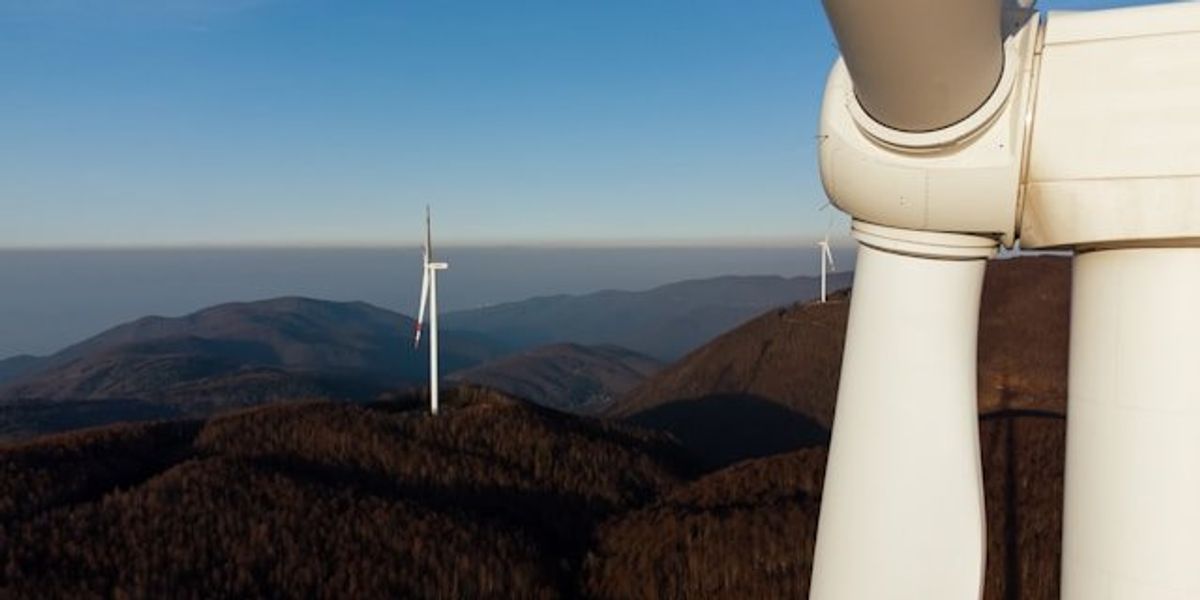 A closeup of a wind turbine situated on a mountain ridgeline.