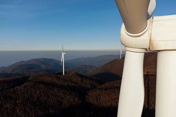 A closeup of a wind turbine situated on a mountain ridgeline.